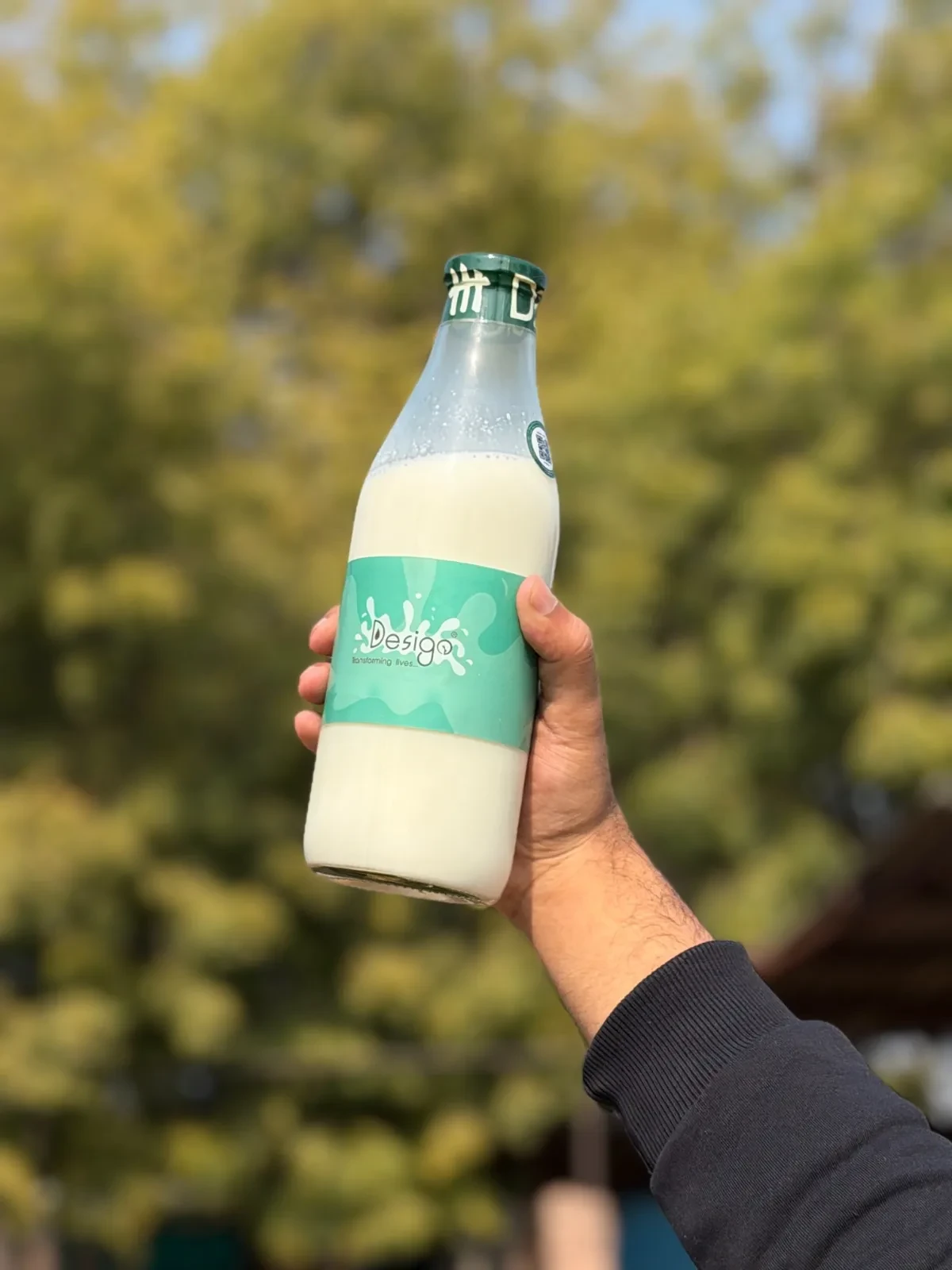A DESIGO® milk bottle held up outdoors against trees
